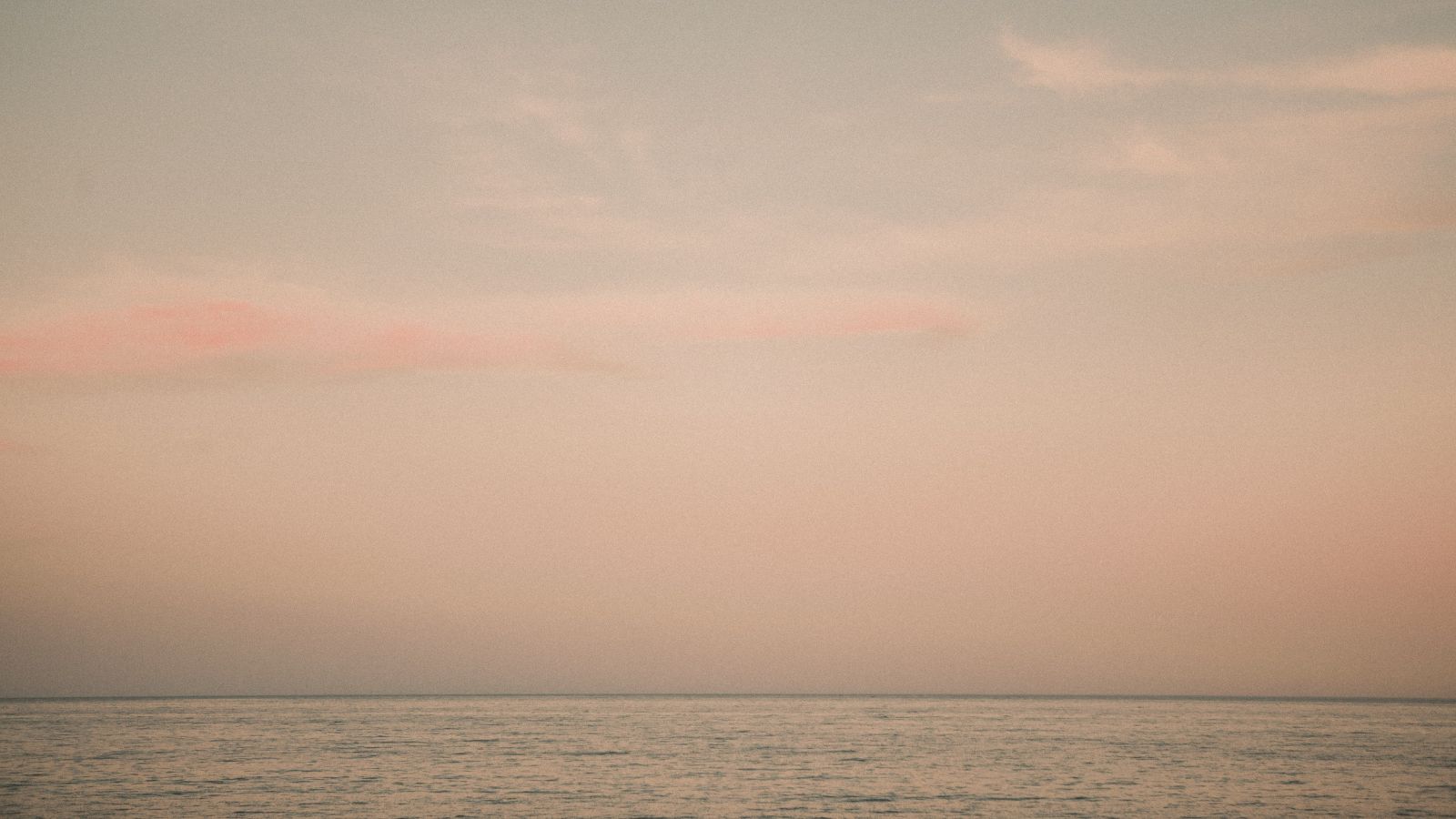 A calm dawn sky in soft pink over a still ocean horizon.